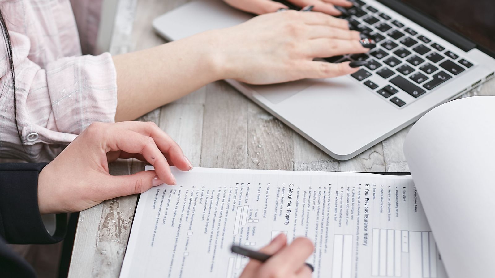 Hands filling out a form next to a laptop